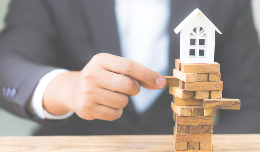 Businessman,hand,holding,wood,block,with,model,white,house.,investment